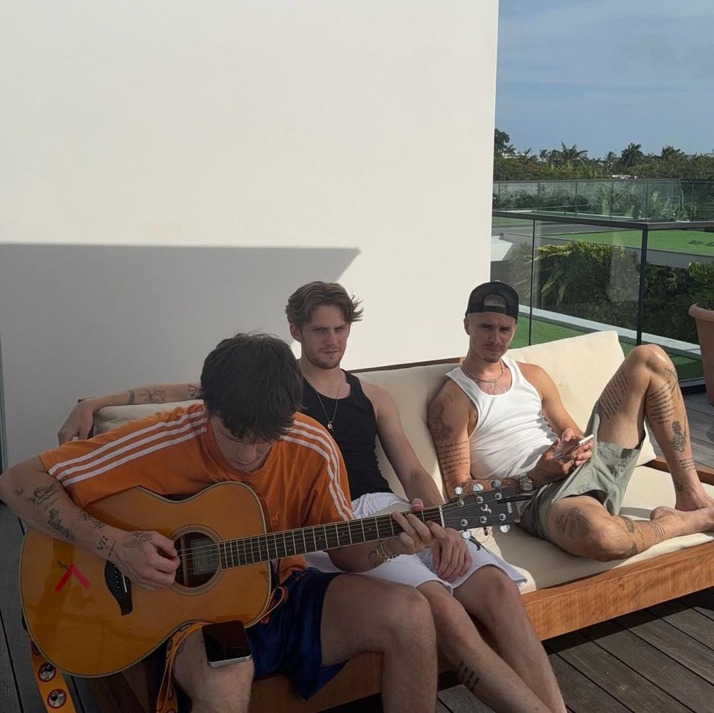 Cruz playing guitar with a friend and Romeo sitting next to him on the decking of the Beckham's family home on Miami Beach