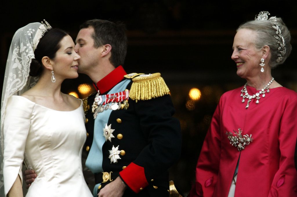 King Frederik kissing Queen Mary on the cheeck while Queen Margrethe looks on