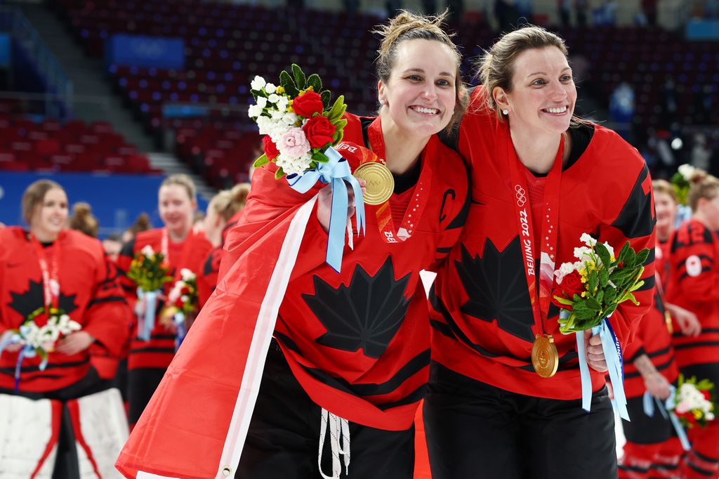 Marie-Philip Poulin et Laura Stacey souriantes, portant leurs médailles d'or et leurs uniformes rouges tout en tenant des fleurs