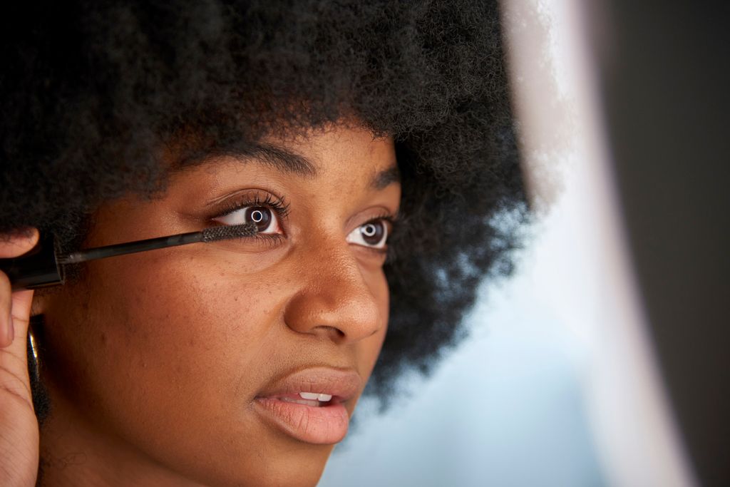 Close-up view of an Afro woman applying mascara on her eyelashes while doing her makeup. Concept of cosmetics, makeup and beauty.