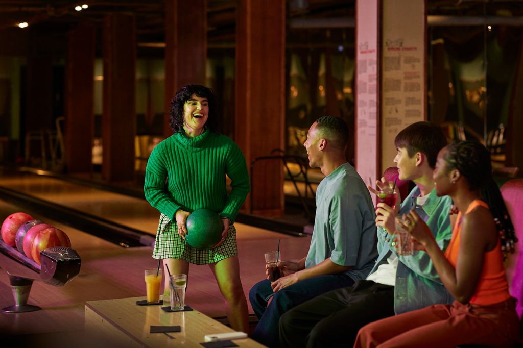 Cheerful woman holding ball while talking with male and female friends at bowling alley