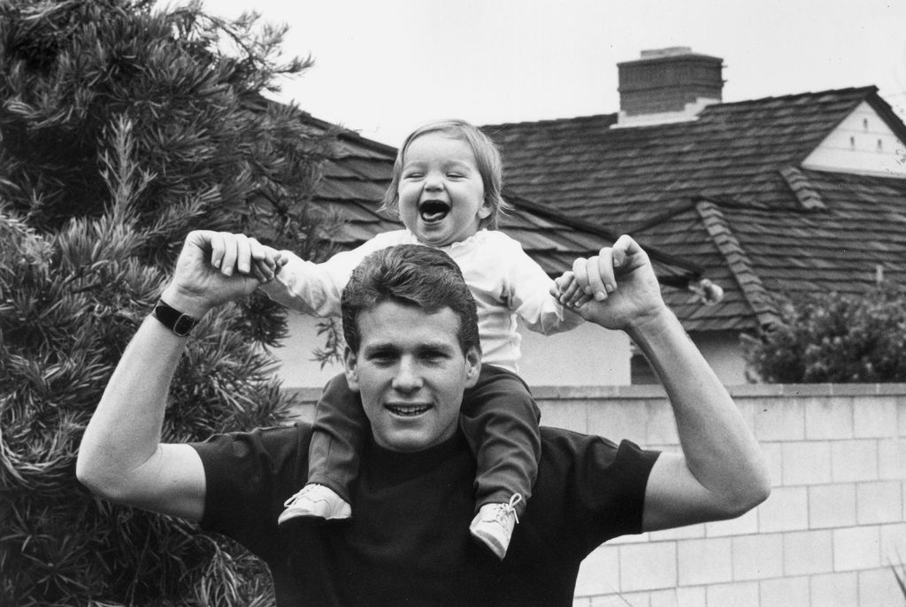 Ryan O'Neal holding his smiling daughter Tatum on his shoulders in front of a house