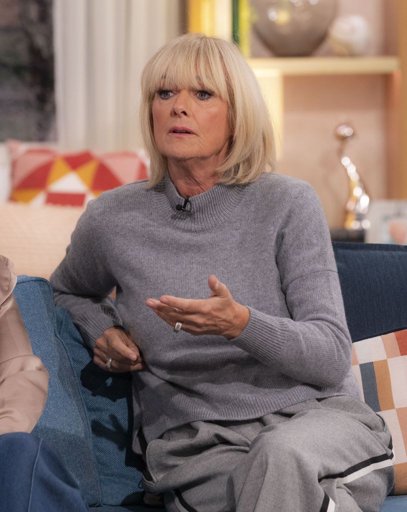 women in grey sweater sat on chair with hand up