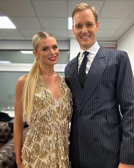 dan wearing a 1920s style pinstripe double breasted suit standing next to his dance parter who wears a gold sequin flapper dress and they both look cheerful