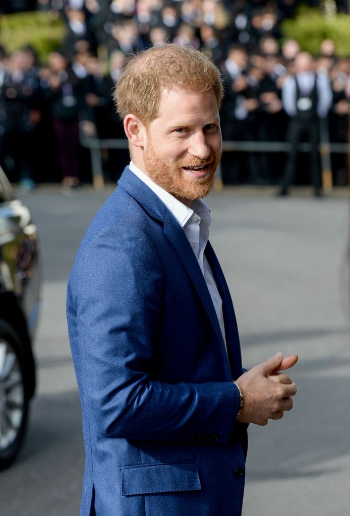 Prince Harry smiling in blue suit as he arrives at Nottingham school