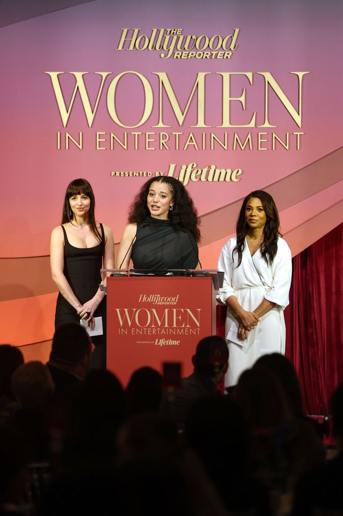 Dakota Johnson, Chase Infiniti and Regina Hall speak on stage at the Women in Entertainment event. The trio present on stage talking into a microphone