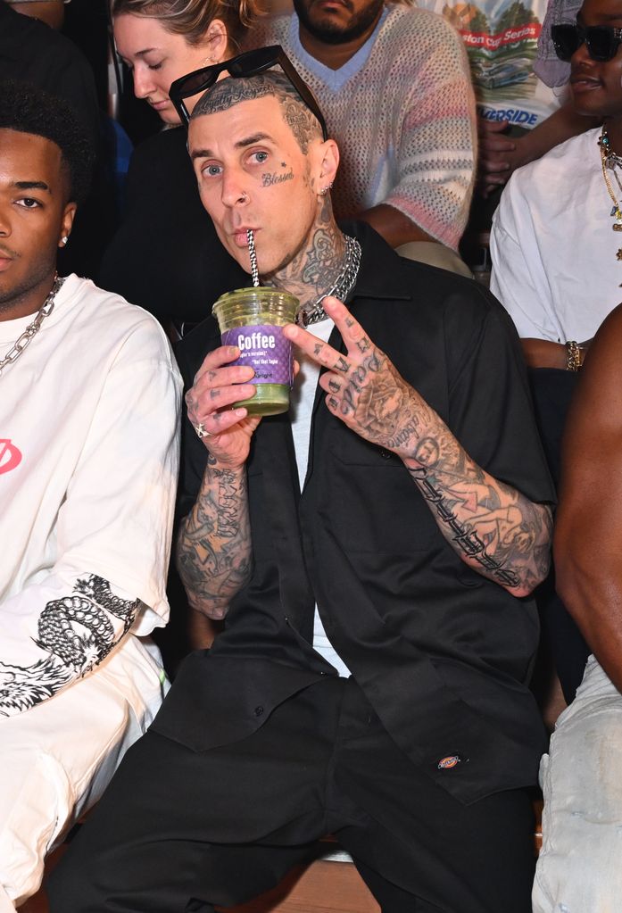Travis Barker drinking a green juice on the FROW at the NAHMIAS SS25 Menswear Show  
