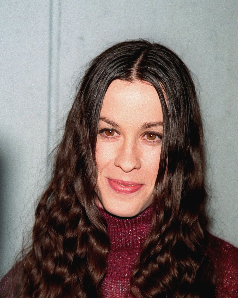 Alanis Morisettle porte ses longs cheveux bruns bouclés et porte un pull à col roulé rouge moucheté.