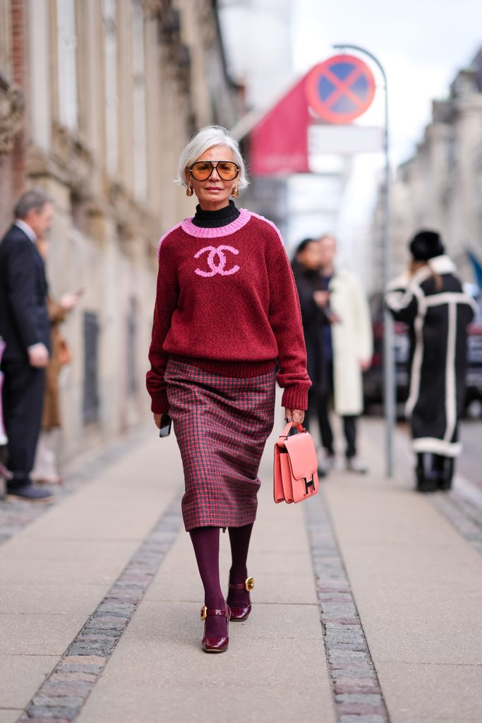 Grece Ghanem wears sunglasses, golden earrings, a black turtleneck pullover , a pink and red Chanel pullover, a red midi checkered / checked pattern printed skirt , burgundy leggings, matching leather shoes, a Hermes pink bag, outside The Garment, during the Copenhagen Fashion Week AW24 on January 31, 2024 in Copenhagen, Denmark