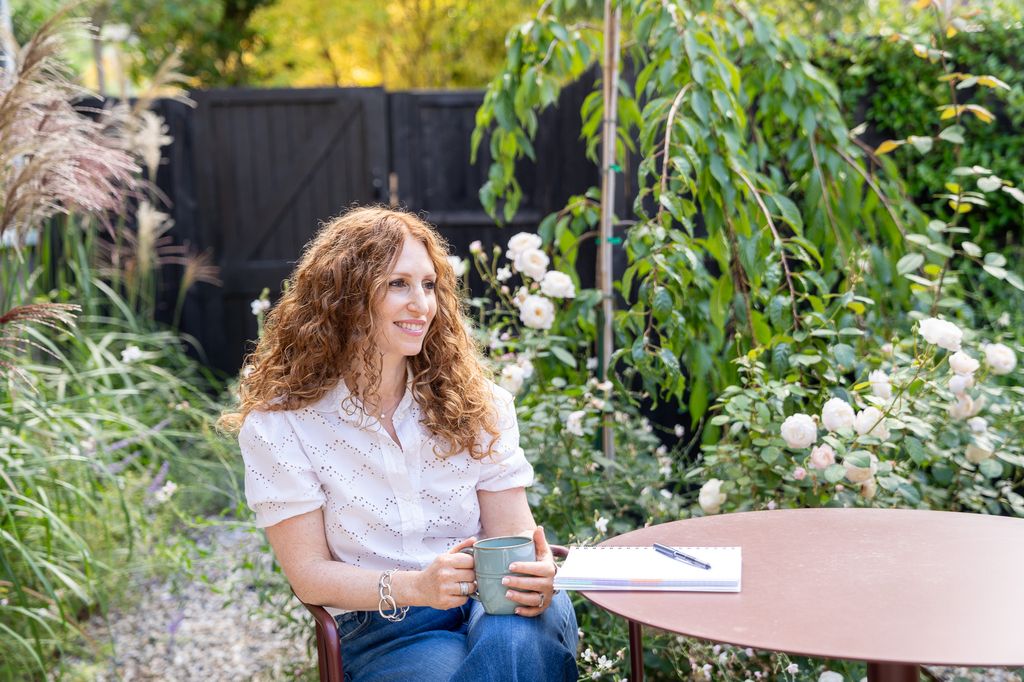 Woman with curly hair sitting in a serene garden with a mug of tea