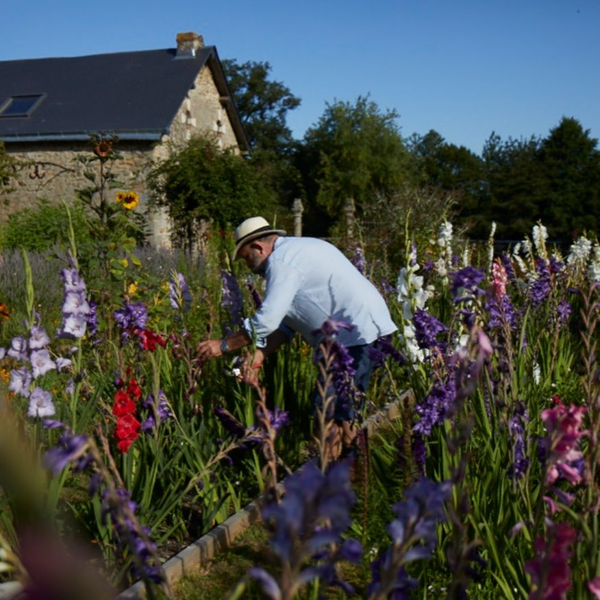 Dick Strawbridge in a blue shirt, jeans and a trilby as he tends to flowers in their garden at French Chateau