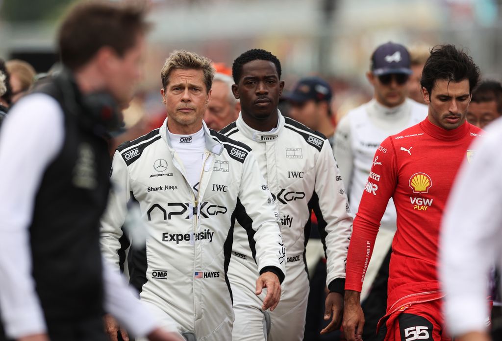 Brad Pitt, star of the upcoming Formula One based movie, Apex, and Damson Idris, co-star of the upcoming Formula One based movie, Apex, walk on the grid in front of Carlos Sainz of Spain driving (55) the Ferrari SF-23 on track during the F1 Grand Prix of 