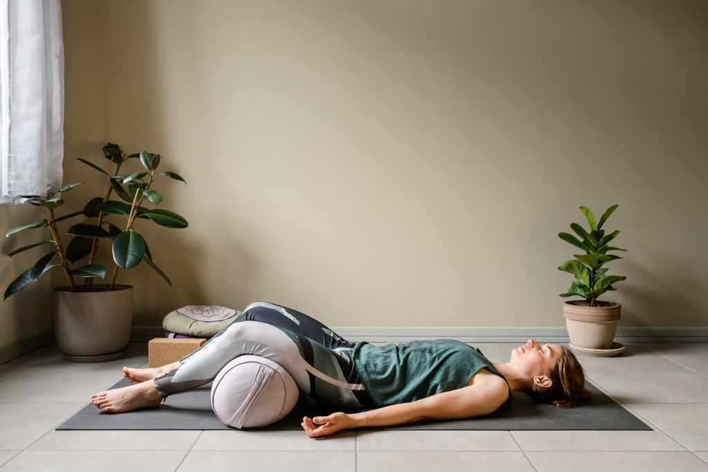 Woman practicing restorative yoga at home: The Corpse, Savasana pose