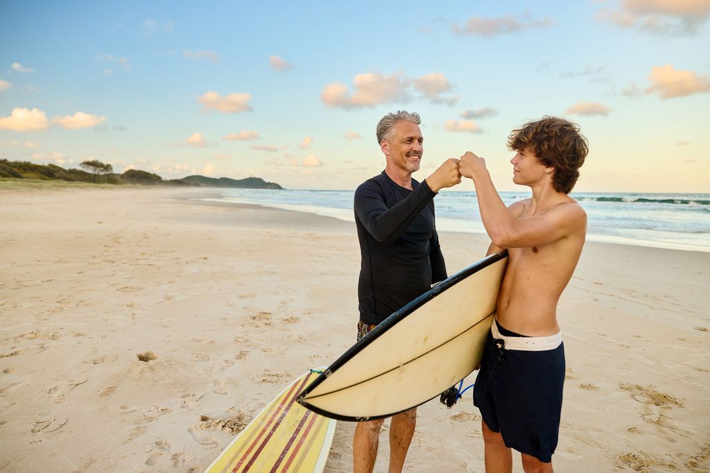 Père et fils tenant des planches de surf sur la plage