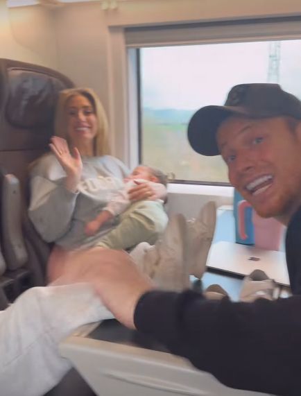 Stacey Solomon holding a baby while on a train with Joe Swash