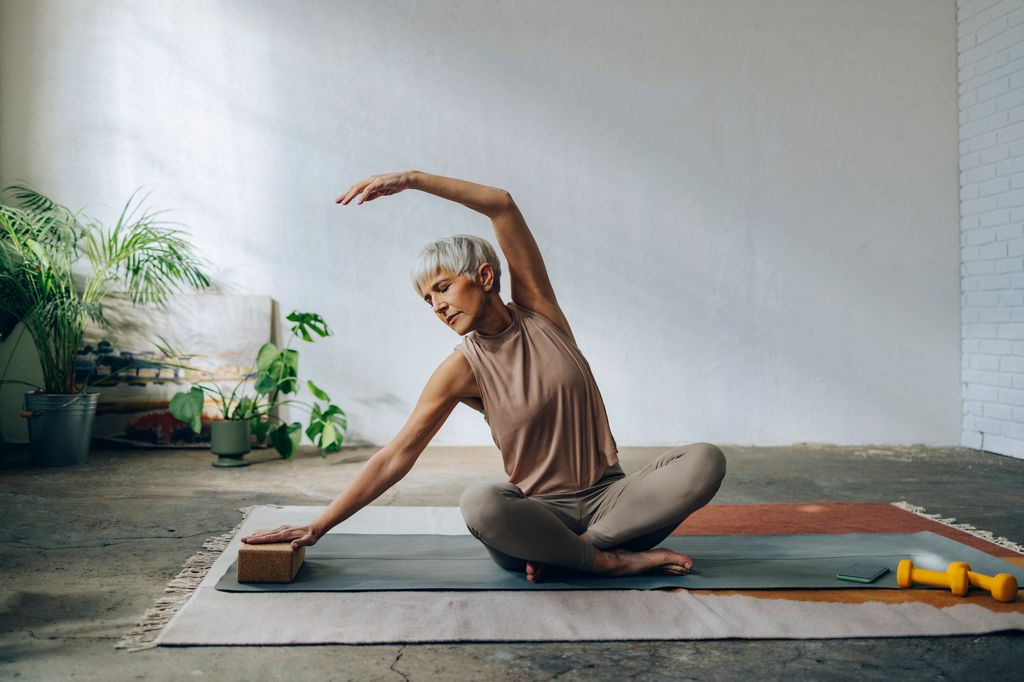 Serious woman in sportswear sitting on a exercise mat and stretching arms.