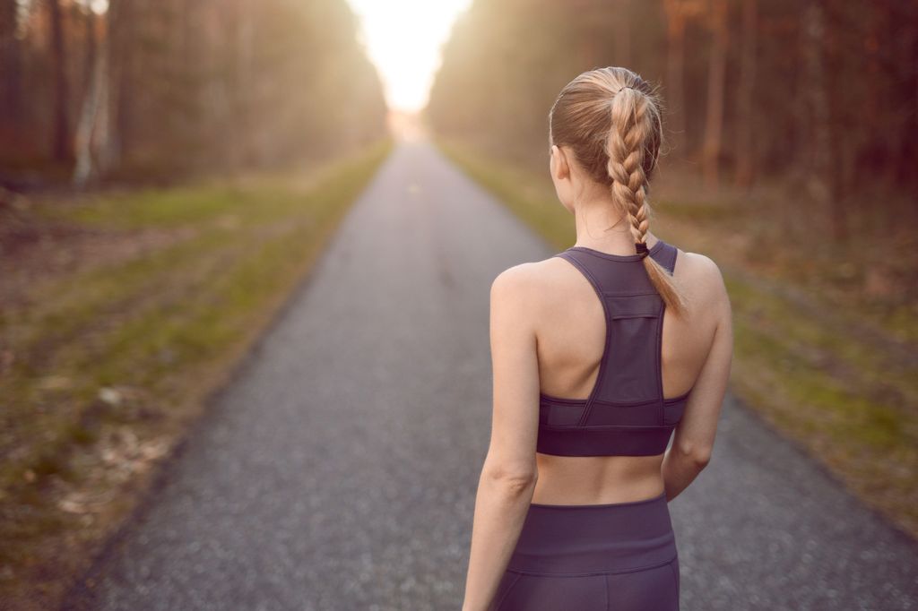 Sporty woman walking at sunrise along a rural road through a dense forest