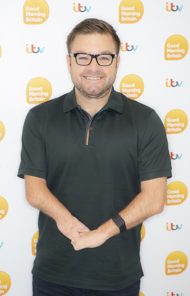 Alex Brooker in front of 'Good Morning Britain' board smiling for camera
