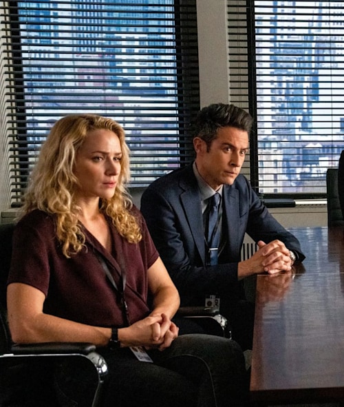 Nina and Scola, both with their hands together, sit at a desk