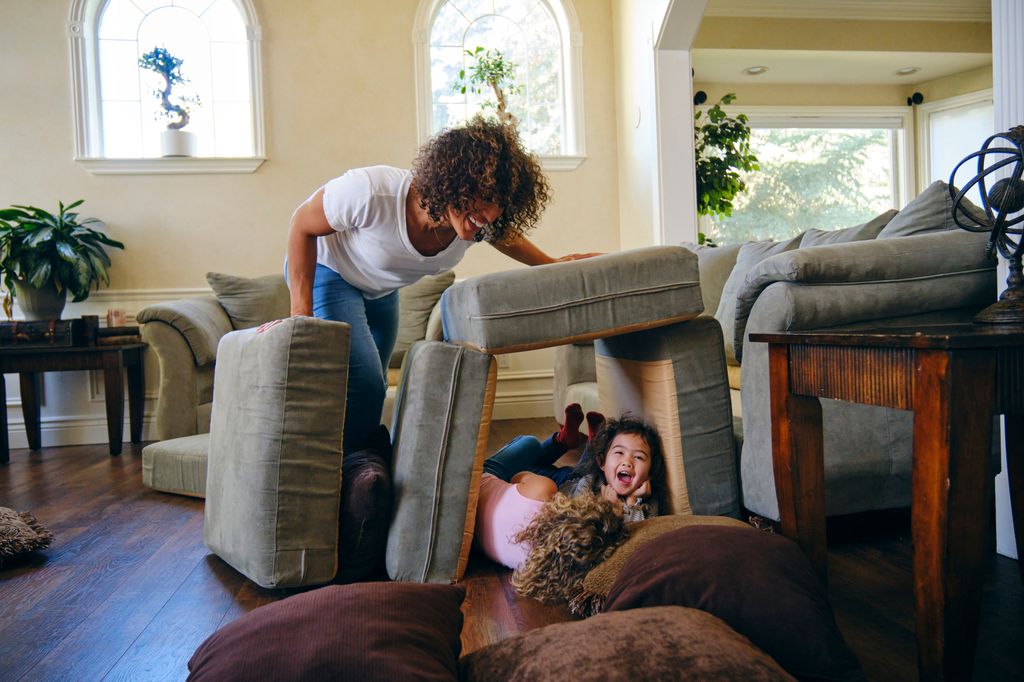deux filles et un parent faisant une tanière à partir de coussins de canapé 