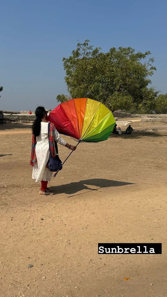 Woman walking in sand with rainbow umbrella