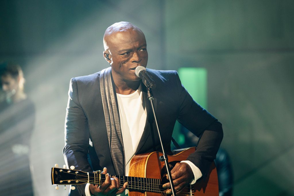 Seal performing on a stage with a guitar and singing into a microphone