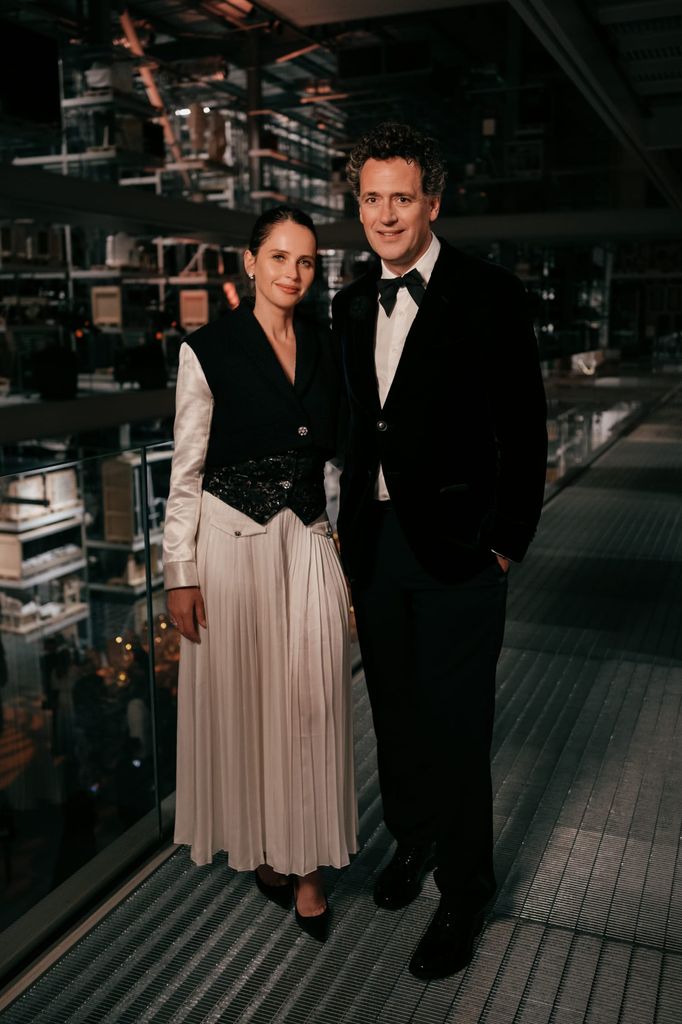 Felicity Jones and Charles Guard attend CHANEL’s 100-year UK celebration at the V&A East Storehouse, with Felicity wearing a long pleated white skirt and cropped jacket and Charles in classic black tie.