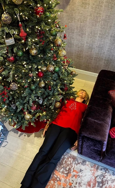 Ruth Langsford wearing red top and black trousers lying under Christmas tree as a joke