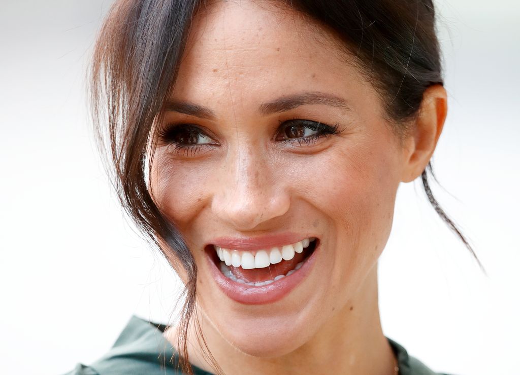 Meghan Markle smiling widely with her hair up
