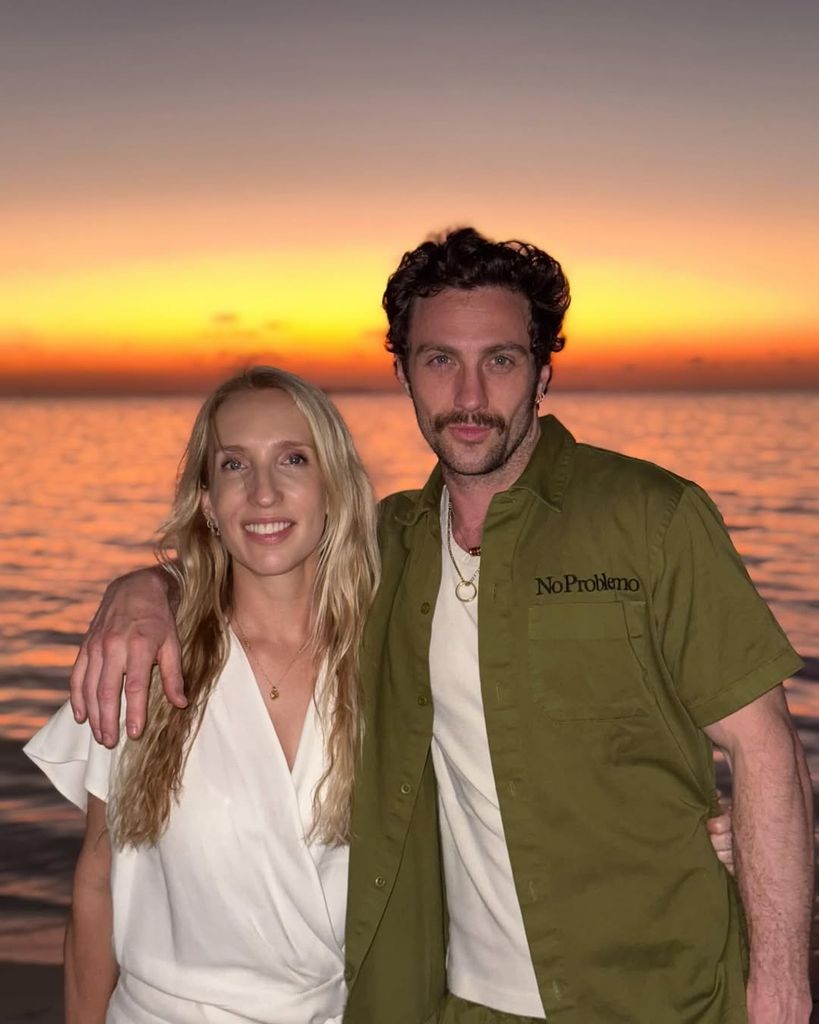 Aaron Taylor-Johnson met son bras autour de sa femme Sam en posant devant un coucher de soleil