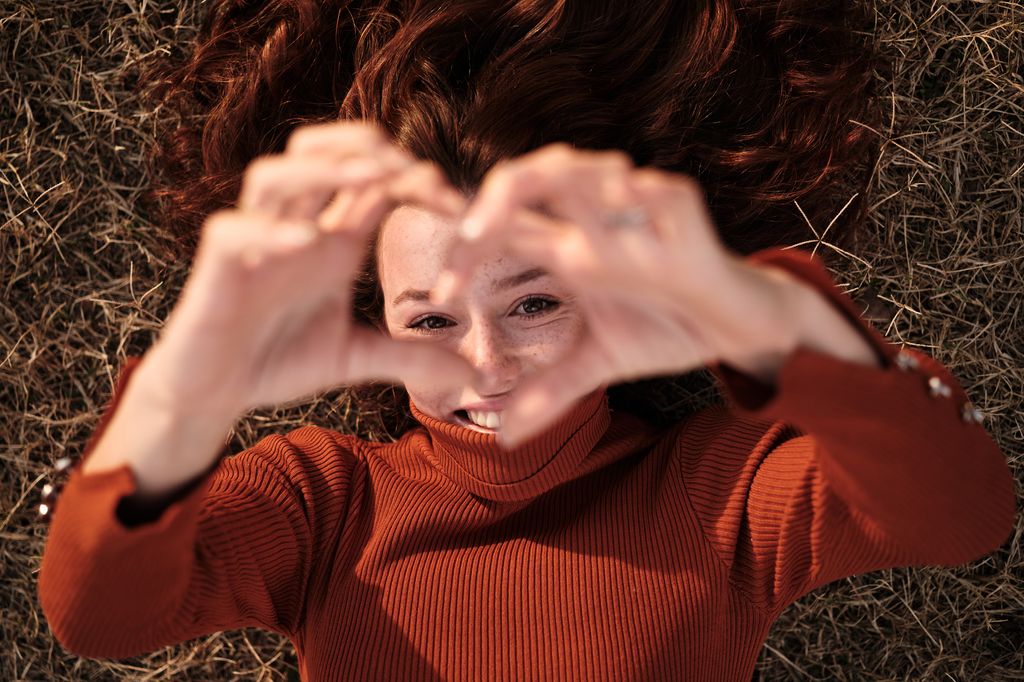 Top view portrait of a beauty woman gesturing the shape of a heart with her hands while lying on the grass in a park