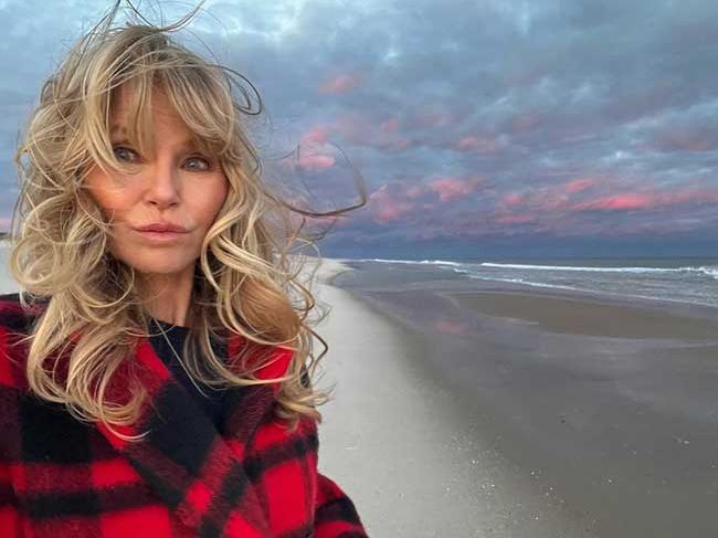Christie poses for a selfie looking windswept on a beach at dusk, there are hints of pink in the clouds
