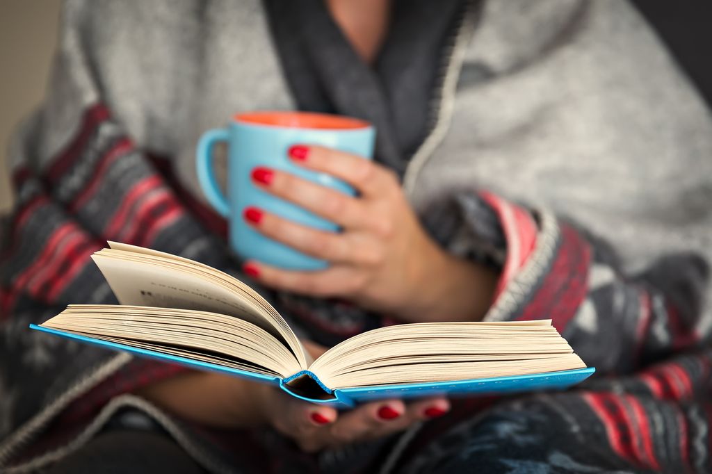 A woman reading a book and drinking from a mug
