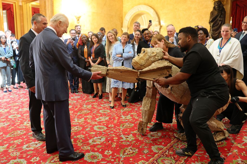 King Charles shakes hand with gorilla puppet in room of people