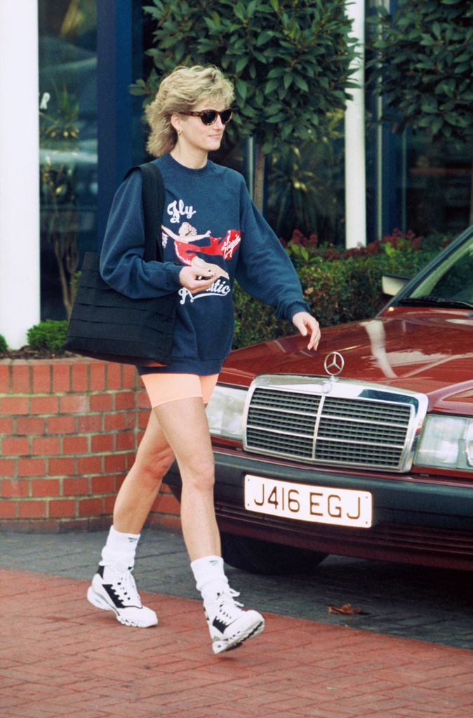 Princess Diana, Princess of Wales styles a navy Virgin Atlantic sweatshirt alongside orange cycling shorts 