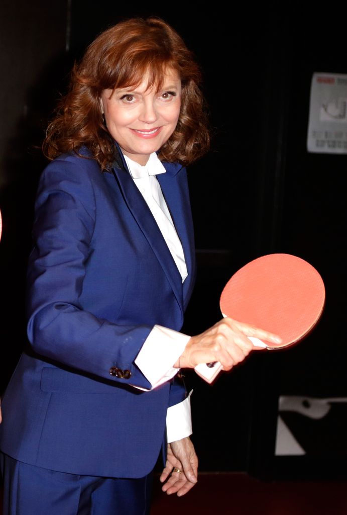Susan Sarandon dans un costume de la Marine, souriant en tenant une raquette de ping-pong