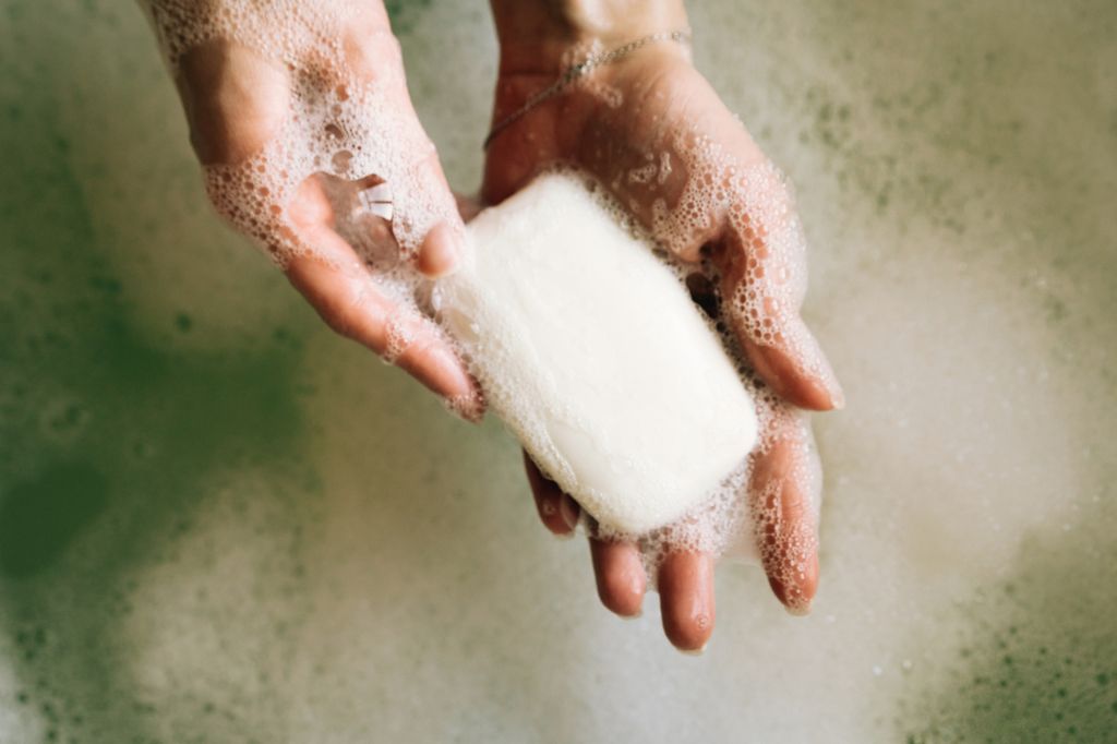 White toilet soap in female hands against the background of a fragrant foam bath 