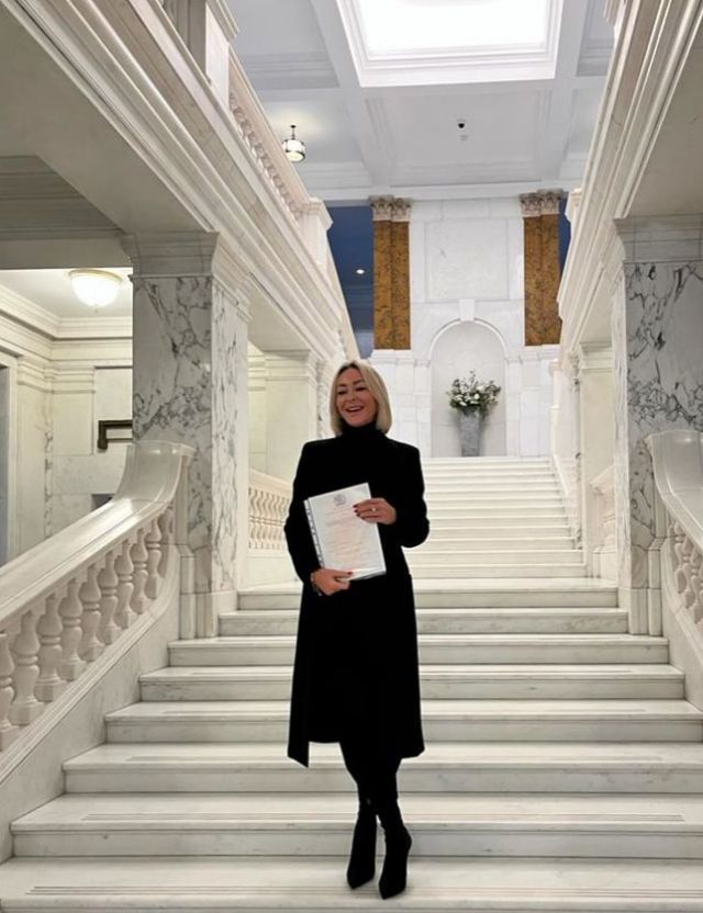 Luba Mushtuk on a set of marble stairs holding a British citizen certificate