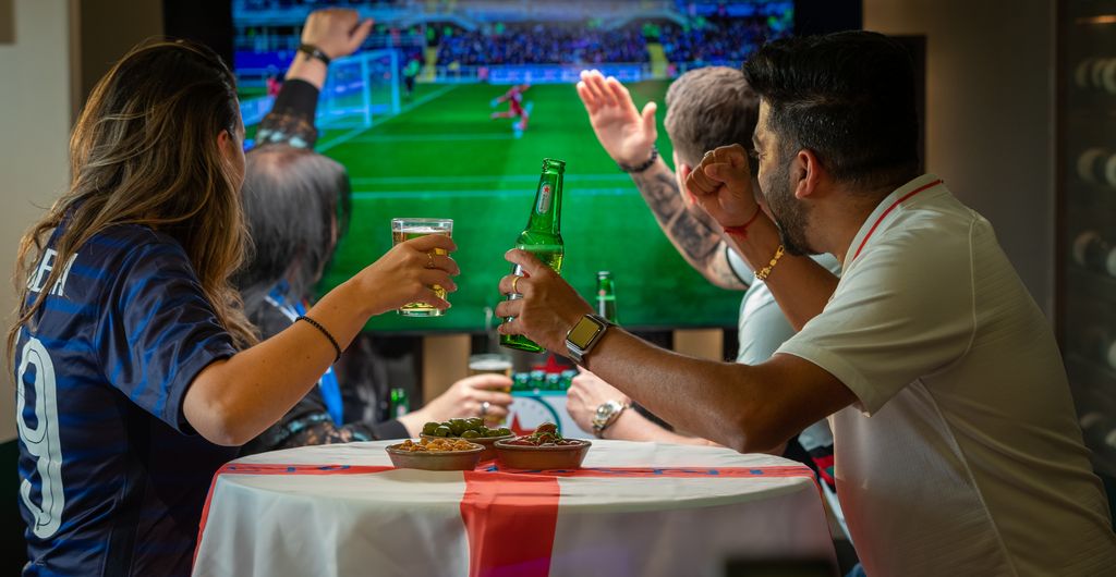 men and women at table cheering on England playing football
