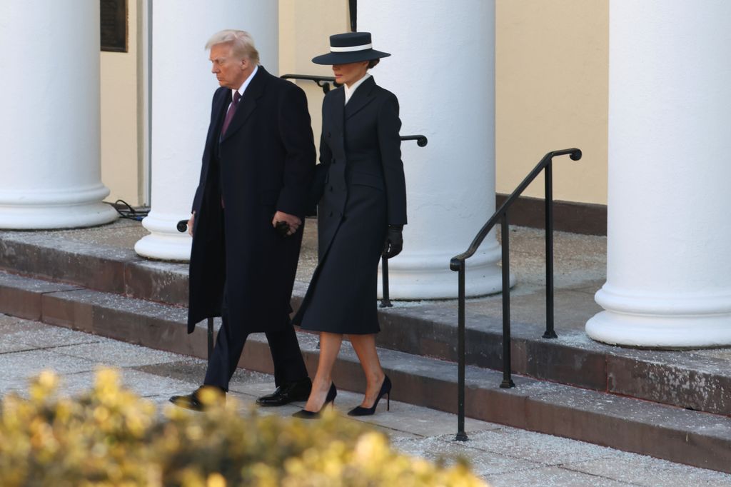 Melania Trump dressed in a sleek navy coat Paired with a dramatic wide-brimmed hat and pointy stilettos walking down the stairs next to husband Donald Trump