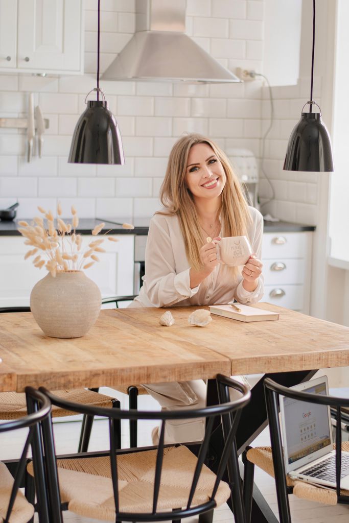 Blonde woman smiling as she drinks a cup of coffee in the kitchen