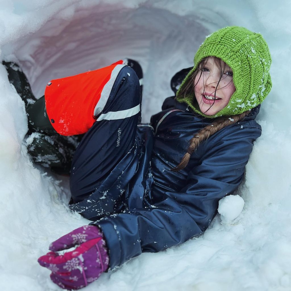 girl sitting in snow cave wearing waterproof gear 