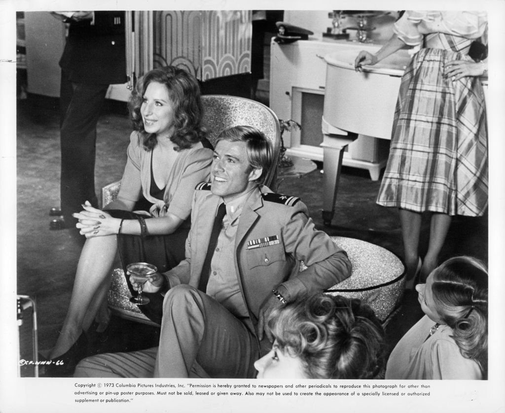 Barbara Streisand and Robert Redford sit smiling looking forward in a scene from the film 'The Way We Were', 1973