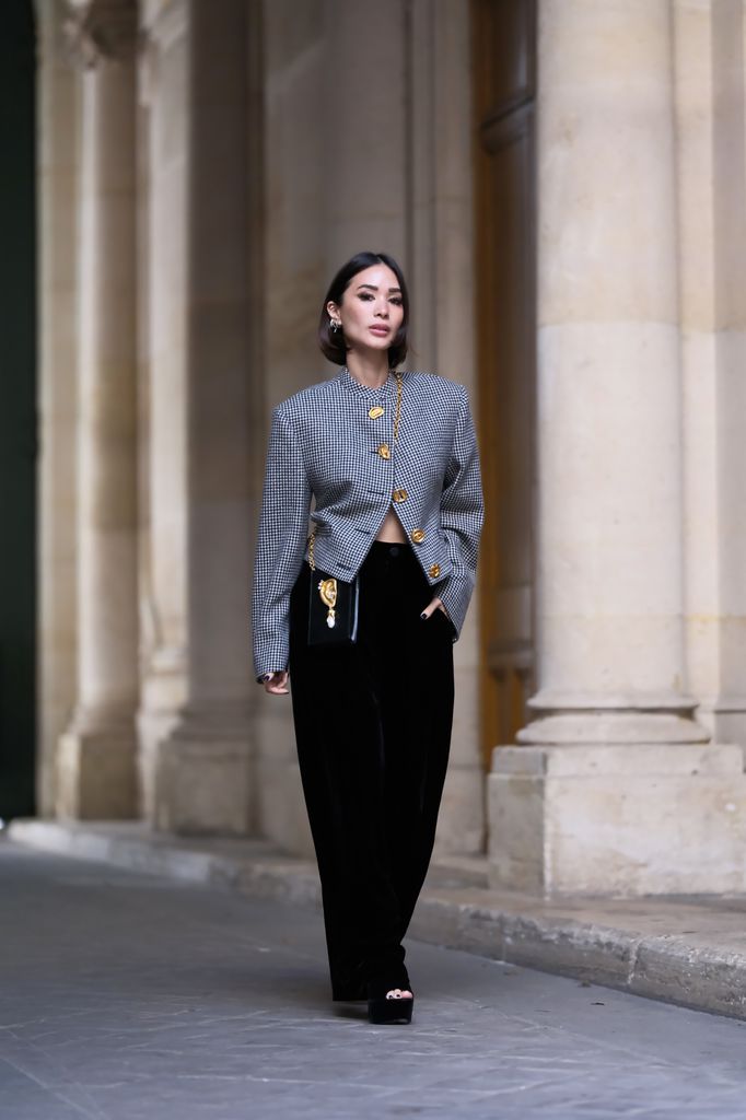 PARIS, FRANCE - OCTOBER 06: Heart Evangelista wears earrings, a black and white houndstooth pattern jacket with shoulder pads and golden buttons, a black rectangular bag with a golden ear detail from Schiaparelli, black high rise wide legs flared pants, platform shoes, during a street style fashion photo session,  on October 06, 2023 in Paris, France. (Photo by Edward Berthelot/Getty Images)