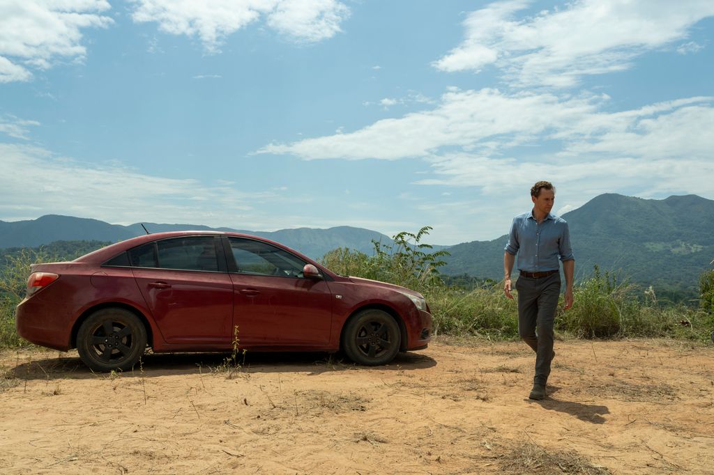 man standing on mountain next to red car