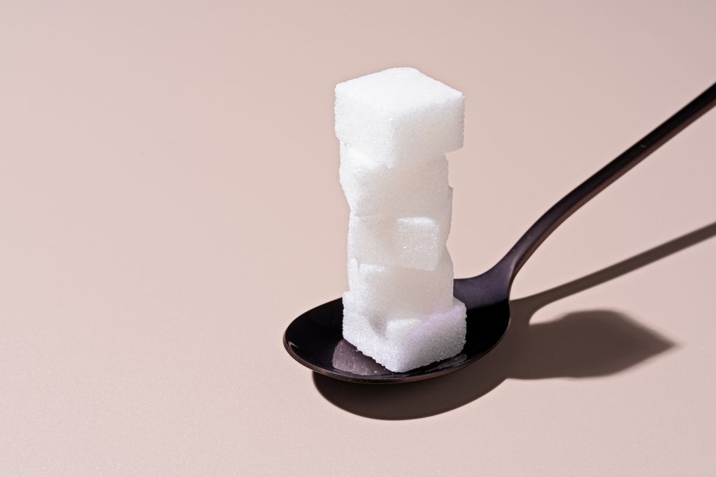 Sugar Cubes Stack High in Spoon on Beige Background.