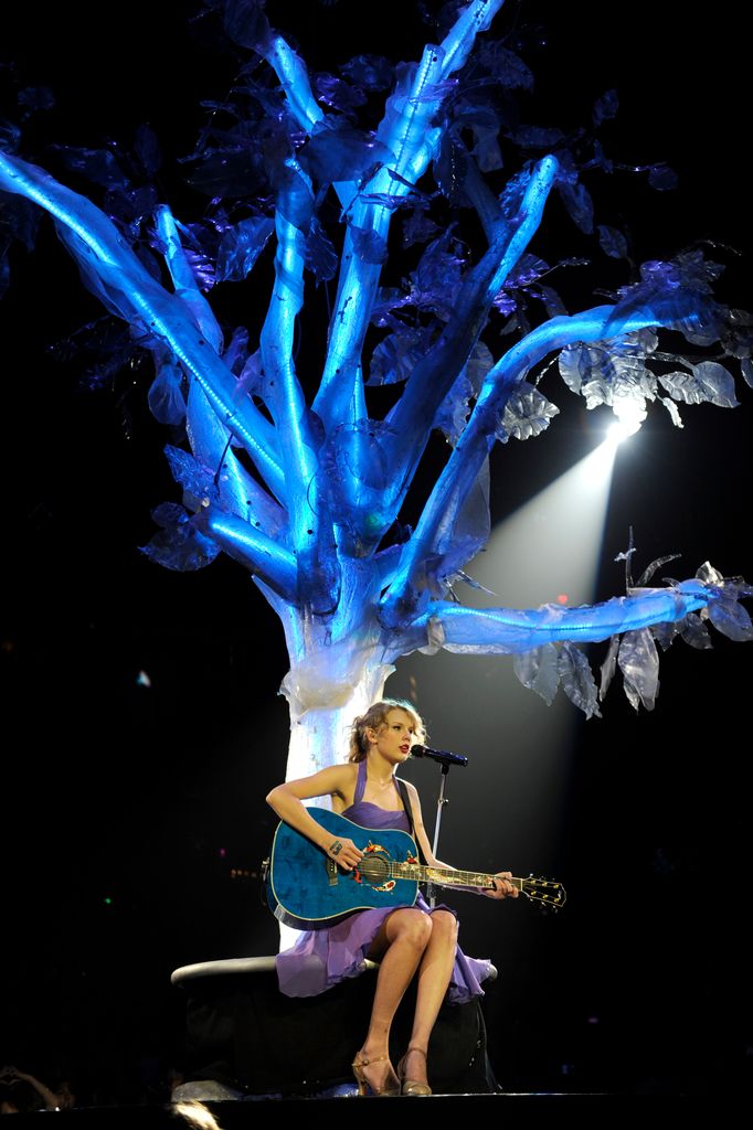 Taylor Swift on stage sitting under purple tree