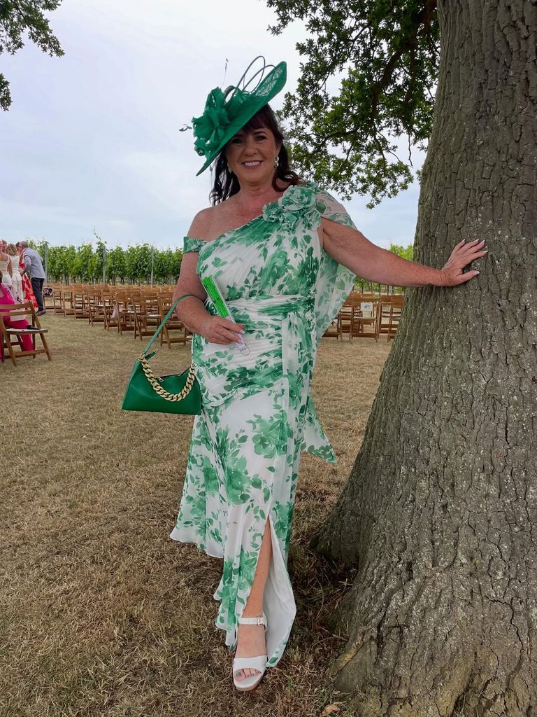 Coleen Nolan leaning against a tree in a green floral dress