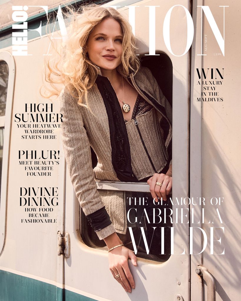 On a second August–September 2025 Hello! Fashion cover, Gabriella Wilde leans from a vintage train carriage in a taupe blazer and corset from Dior, her voluminous curls and luxe De Beers jewellery capturing timeless travel glamour.