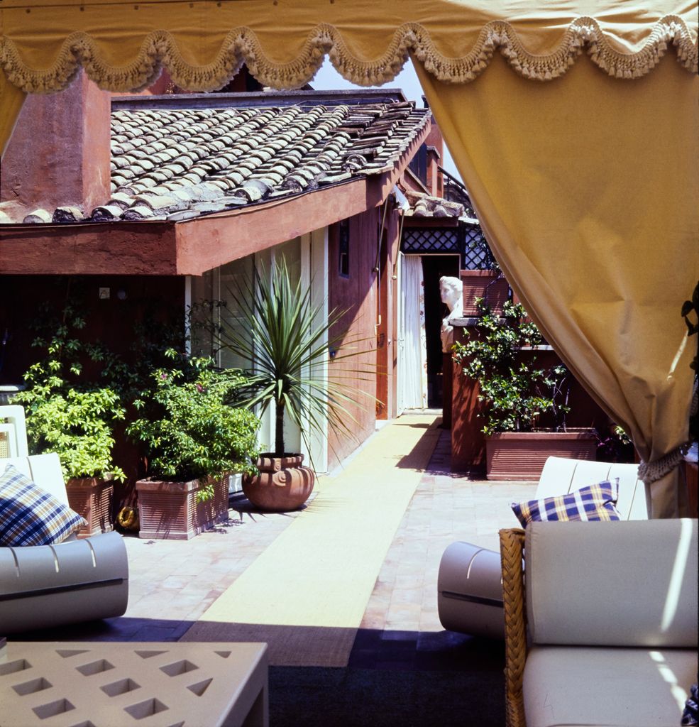 View of the terra-cotta tiled roof of Valentino's Rome apartment, from a yellow sailcloth roof tent. The roof's accoutrements include a potted palm, a neoclassical bust, and a pair of modernist chairs. (Horst P. Horst/Conde Nast via Getty Images)